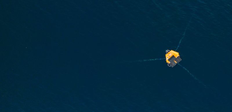 Miramare Station, aerial photo, showing a dark ocean with a yellow buoy with three cables under the water extending from buoy.